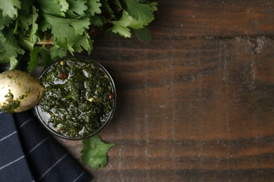 Photo of Tasty cilantro sauce in bowl on wooden table, flat lay. Space for text
