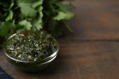 Photo of Tasty cilantro sauce in bowl on wooden table, closeup. Space for text