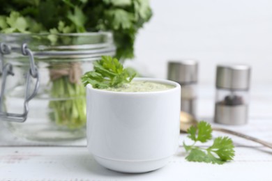 Photo of Tasty cilantro sauce in bowl on white wooden table, closeup