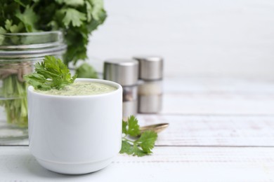 Photo of Tasty cilantro sauce in bowl on white wooden table, closeup. Space for text