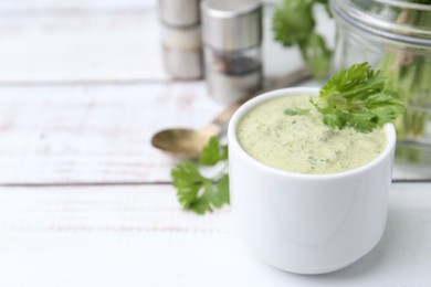 Photo of Tasty cilantro sauce in bowl on white wooden table, closeup. Space for text