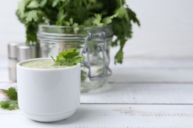 Photo of Tasty cilantro sauce in bowl on white wooden table, closeup. Space for text