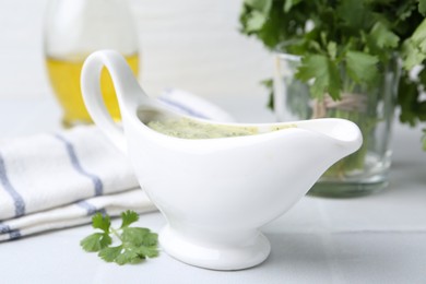 Photo of Tasty cilantro sauce in gravy boat on light tiled table, closeup