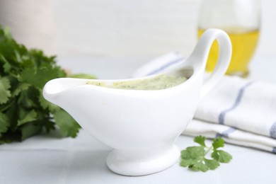 Photo of Tasty cilantro sauce in gravy boat on light tiled table, closeup