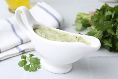 Photo of Tasty cilantro sauce in gravy boat on light tiled table, closeup
