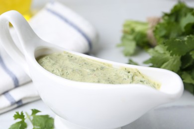 Photo of Tasty cilantro sauce in gravy boat on light table, closeup