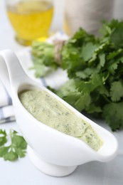 Photo of Tasty cilantro sauce in gravy boat on light table, closeup