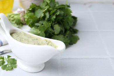 Photo of Tasty cilantro sauce in gravy boat on light tiled table, closeup