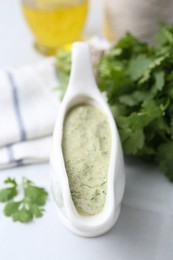 Photo of Tasty cilantro sauce in gravy boat on light table, closeup