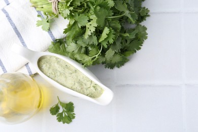 Photo of Tasty cilantro sauce in gravy boat on light tiled table, flat lay