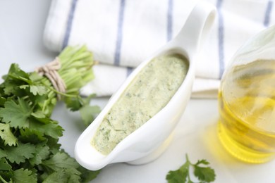 Photo of Tasty cilantro sauce in gravy boat on light table, closeup