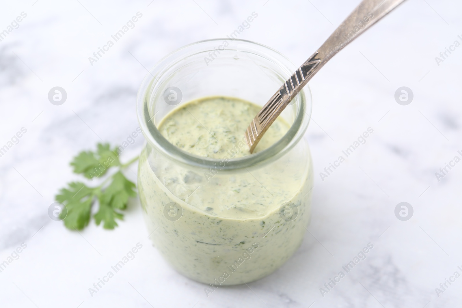 Tasty cilantro sauce and spoon in jar on light marble table, closeup Photo of Tasty cilantro sauce and spoon in jar on light marble table, closeup