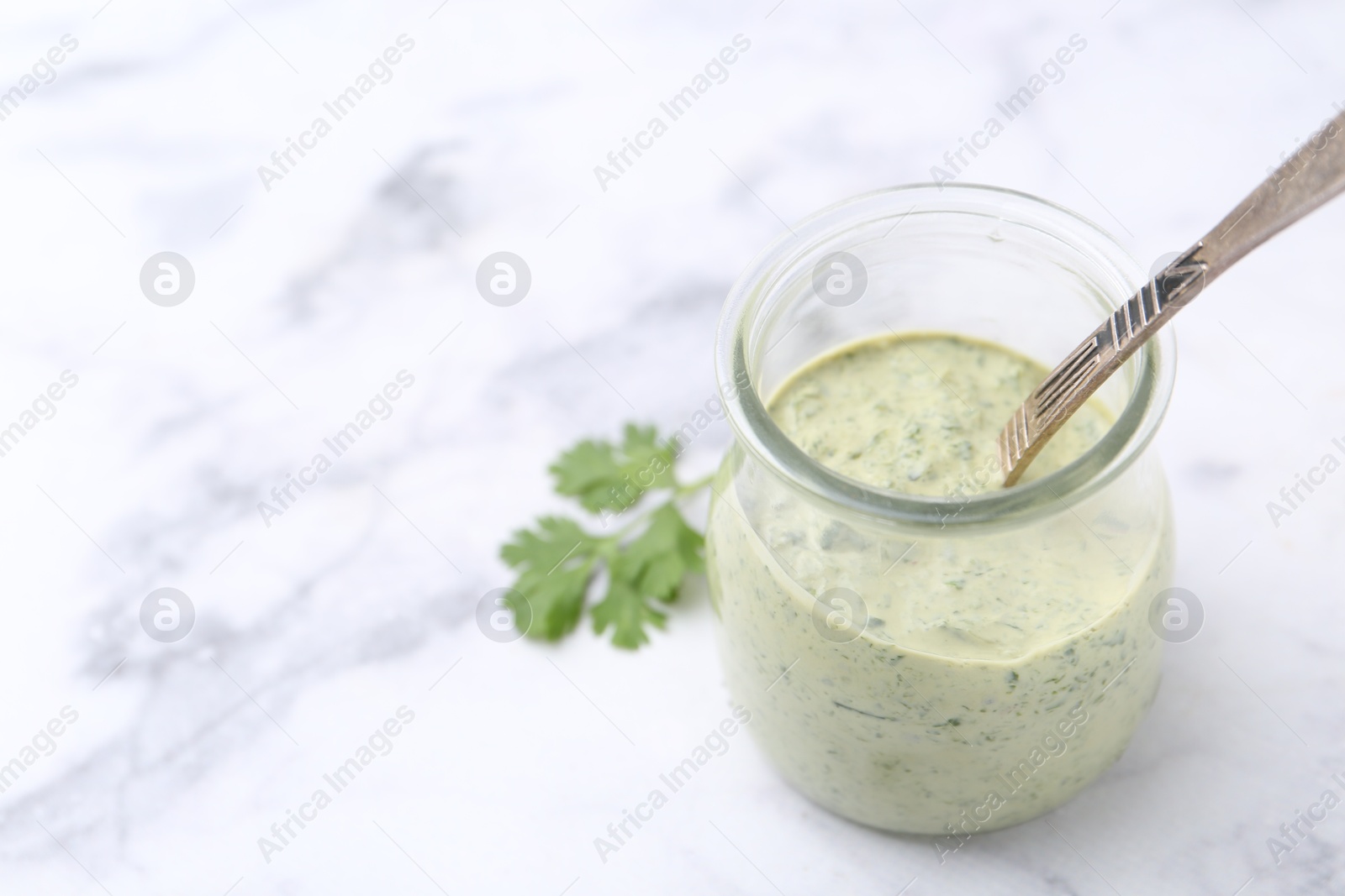 Tasty cilantro sauce and spoon in jar on light marble table, closeup. Space for text Photo of Tasty cilantro sauce and spoon in jar on light marble table, closeup. Space for text