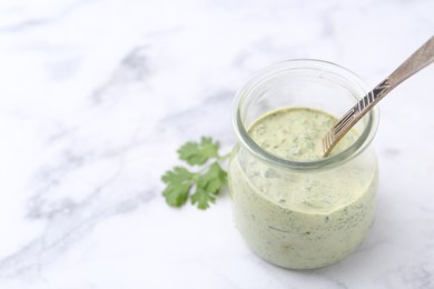 Photo of Tasty cilantro sauce and spoon in jar on light marble table, closeup. Space for text