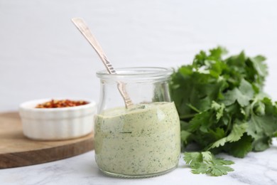 Photo of Tasty cilantro sauce and spoon in jar on light marble table, closeup