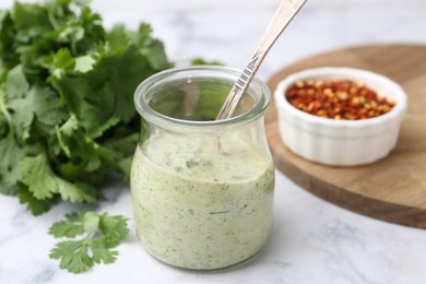 Photo of Tasty cilantro sauce and spoon in jar on light marble table, closeup