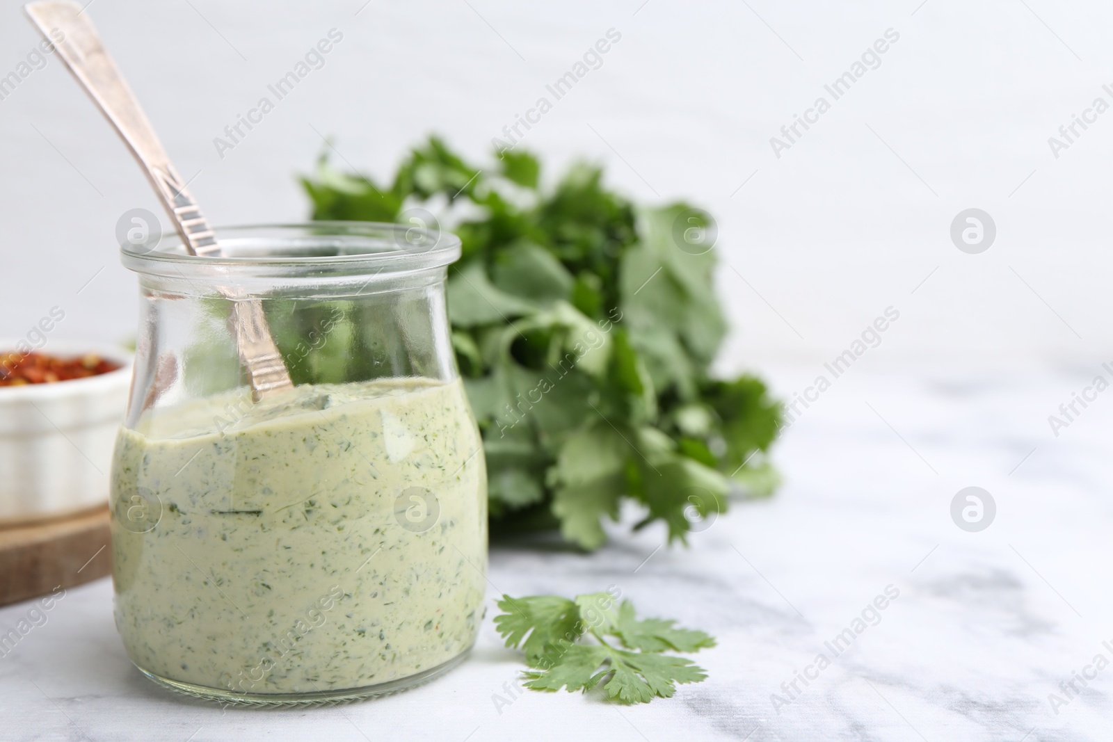 Tasty cilantro sauce and spoon in jar on light marble table, closeup. Space for text Photo of Tasty cilantro sauce and spoon in jar on light marble table, closeup. Space for text