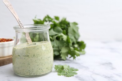 Photo of Tasty cilantro sauce and spoon in jar on light marble table, closeup. Space for text