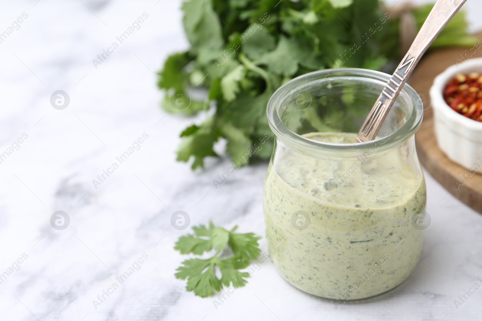 Tasty cilantro sauce and spoon in jar on light marble table, closeup. Space for text Photo of Tasty cilantro sauce and spoon in jar on light marble table, closeup. Space for text