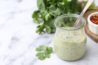 Photo of Tasty cilantro sauce and spoon in jar on light marble table, closeup. Space for text