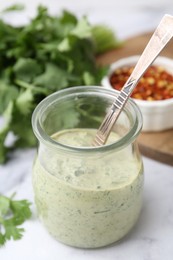 Photo of Tasty cilantro sauce and spoon in jar on light table, closeup