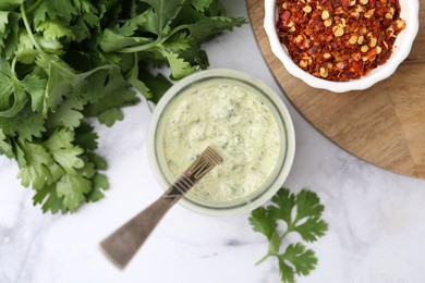 Photo of Tasty cilantro sauce in jar and spices on light marble table, flat lay