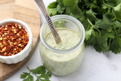 Photo of Tasty cilantro sauce and spoon in jar on light table, closeup
