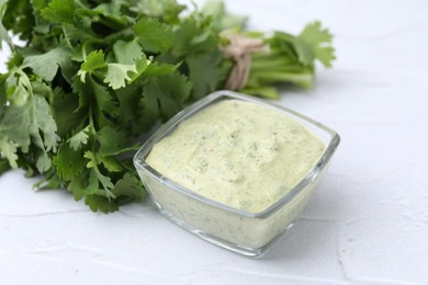 Photo of Tasty cilantro sauce in bowl on light textured table, closeup