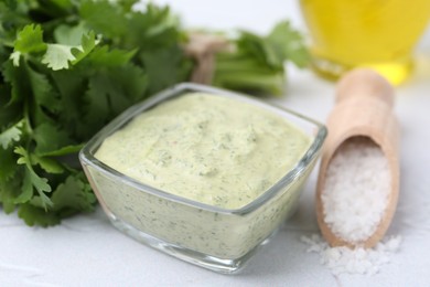 Photo of Tasty cilantro sauce in bowl and salt on light textured table, closeup