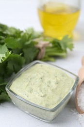 Photo of Tasty cilantro sauce in bowl and salt on light textured table, closeup
