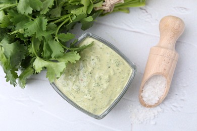 Photo of Tasty cilantro sauce in bowl and salt on light textured table, flat lay