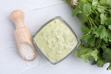 Photo of Tasty cilantro sauce in bowl and salt on light textured table, flat lay
