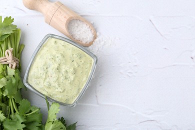 Photo of Tasty cilantro sauce in bowl and salt on light textured table, flat lay. Space for text