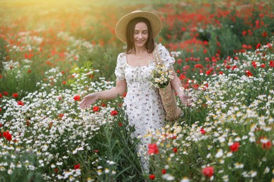 Photo of Smiling woman in hat with bag of chamomile flowers walking in wildflower meadow