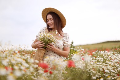 Photo of Smiling woman in hat with bag of chamomile flowers in wildflower meadow