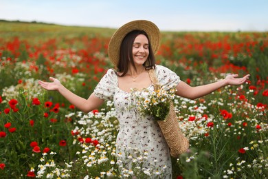 Photo of Smiling woman in hat with bag of chamomile flowers enjoying nature in wildflower meadow