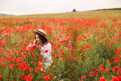 Photo of Beautiful woman in hat sniffing red poppy flowers in wildflower meadow