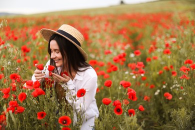 Photo of Smiling woman in hat sniffing red poppy flowers in wildflower meadow