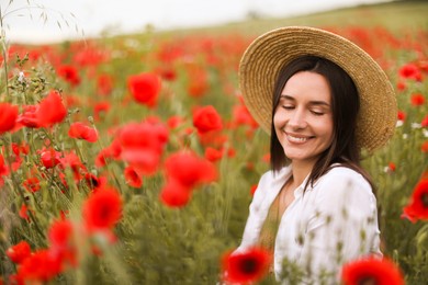 Photo of Smiling woman in hat among red poppy flowers in wildflower meadow
