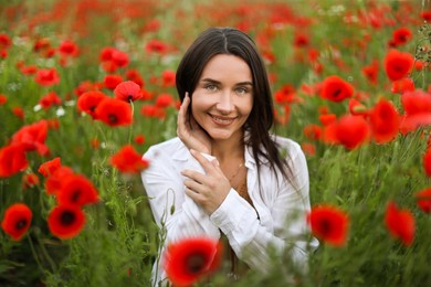 Photo of Portrait of smiling woman among red poppy flowers in wildflower meadow