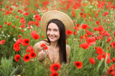 Photo of Portrait of smiling woman in hat among red poppy flowers in wildflower meadow