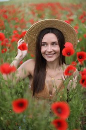 Photo of Smiling woman in hat among red poppy flowers in wildflower meadow