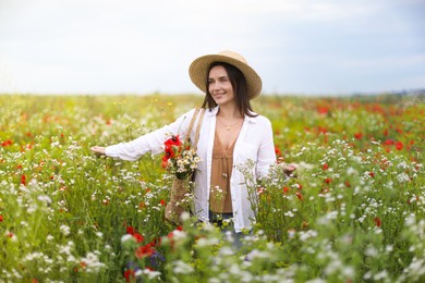Photo of Smiling woman in hat with bag of flowers walking in wildflower meadow