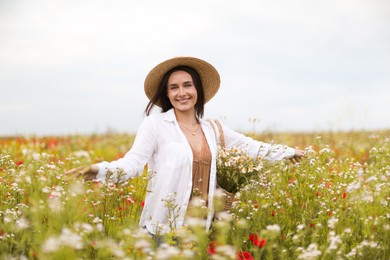 Photo of Smiling woman in hat with bag of chamomile flowers walking in wildflower meadow