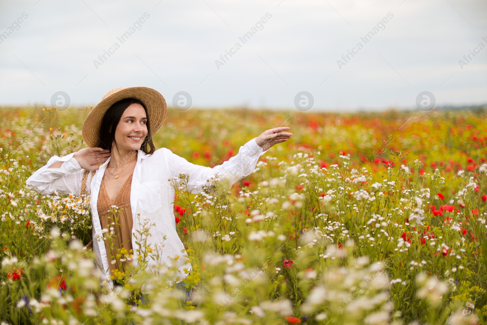 Photo of Smiling woman in hat walking in wildflower meadow