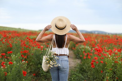 Photo of Woman in hat with bag of chamomile flowers in wildflower meadow, back view