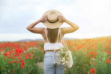 Photo of Woman in hat with bag of chamomile flowers in wildflower meadow, back view