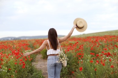 Photo of Woman with hat and bag of chamomile flowers in wildflower meadow, back view