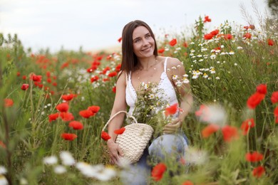 Photo of Smiling woman in hat with bag of chamomile flowers in wildflower meadow