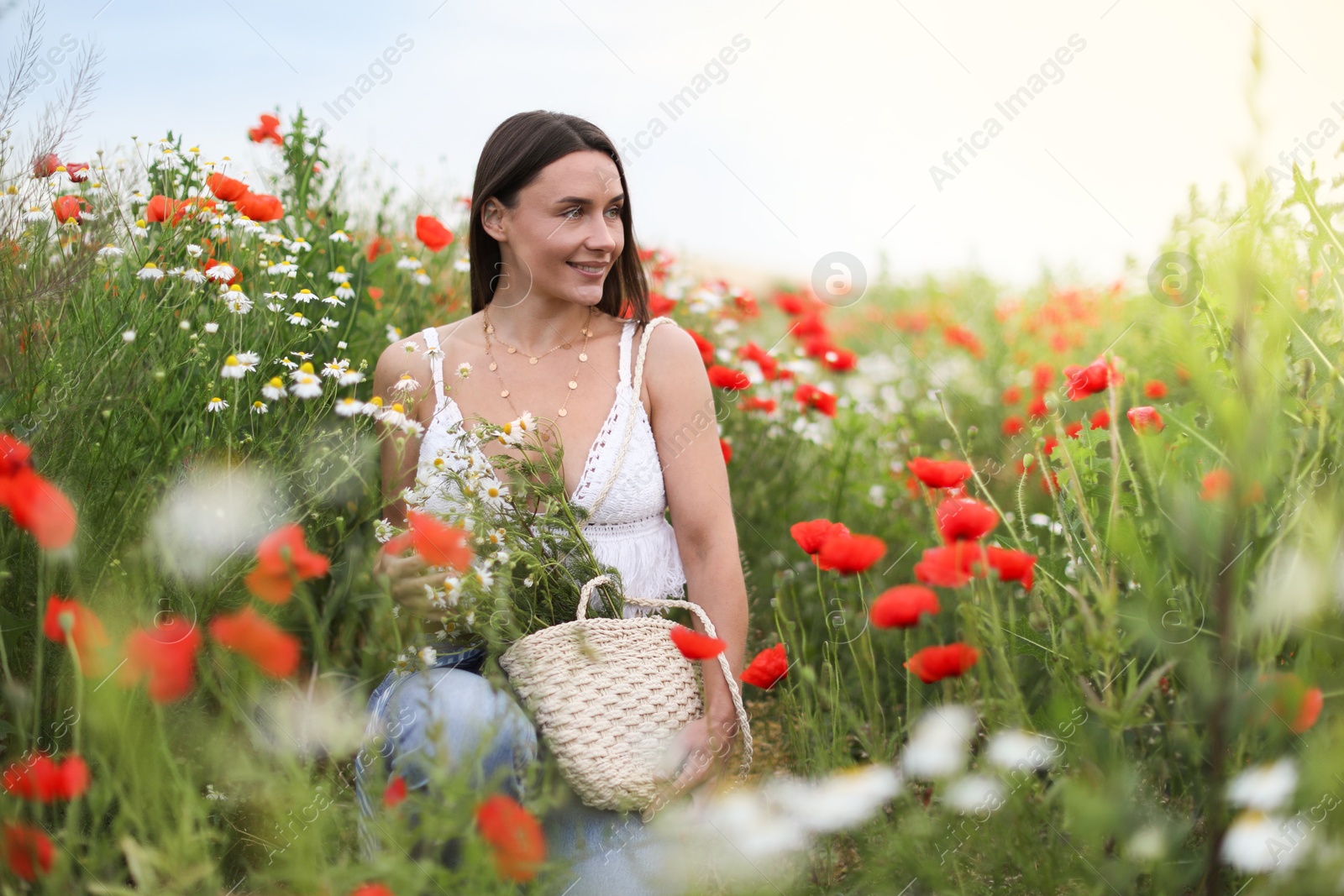 Smiling woman in hat with bag of chamomile flowers in wildflower meadow Photo of Smiling woman in hat with bag of chamomile flowers in wildflower meadow